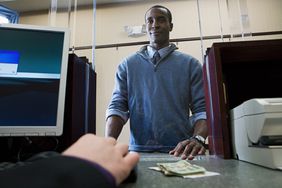Man stands at bank teller paying for a money order with cash
