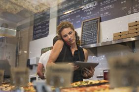 Woman on phone in bakery looking at tablet