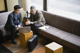 Two businessmen in suits look at laptop in lounge