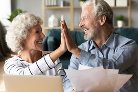 Smiling senior couple at home with paperwork and laptop