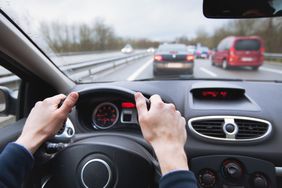Close up of a person's hands on a steering wheel of a car driving on a highway for business.