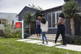 A real estate agent greets two women outside of a house that's for sale.