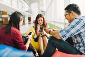Three Asian college students or coworkers using smartphones together. 