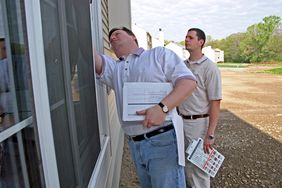Man inspects condition of window exterior while another man watches
