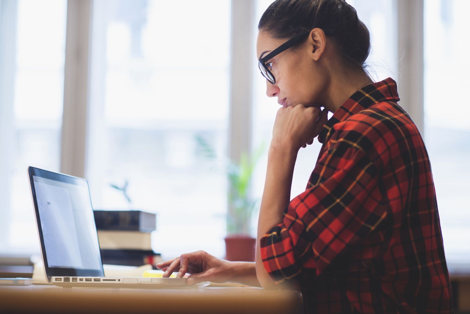 A woman in a red plaid shirt working at a laptop