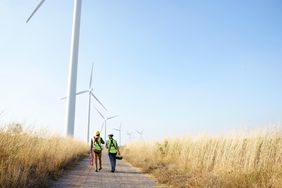 Two workers walk down a dirt path along a line of turbine windmills.