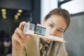 A woman holds up a model of a sleek home and looks closely at it.