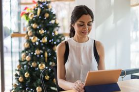 person in a tank top sitting on computer in front of a Christmas tree