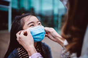 Mom helping her daughter to wear medical face mask