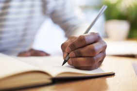 Close up of a man's left hand writing in a notebook with a pen