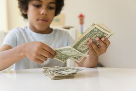A young boy counts dollar bills on a table.