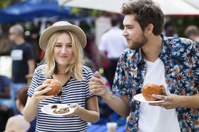 A young couple enjoy street food, and one another's company, at an outdoor market.