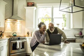 A couple looks at a laptop in their bright kitchen