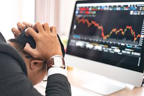Trader clutching his head as he sits before computer monitor showing market prices