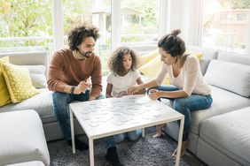 A family plays a board game in a living room.