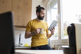 Person holding coffee mug looks at digital tablet in kitchen