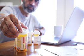 Man reaching for bottles of prescription drugs on a home table