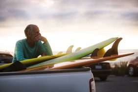 A boomer leans on a stack of surfboards in the back of a pickup after a long day of surfing and wonders if he should have saved more and surfed less.