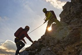 A mountaineer helps a friend climb a rocky slope.