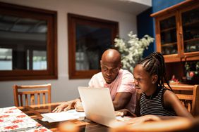 father and daughter sitting at kitchen counter discussing finances in front of computer