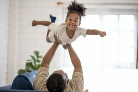 A father hoists his smiling young daughter aloft.