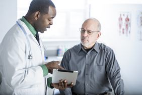 Doctor with digital tablet talks to patient in exam room