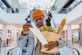 Surprised black man looks at receipt total with food in mall.