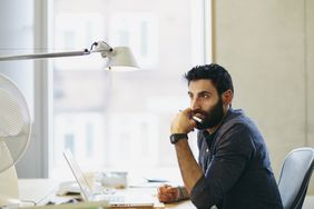 Bearded man thinking before laptop with pen in his hand