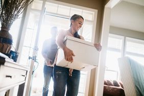 A woman carries a moving box into a house