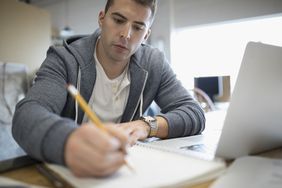 Focused creative businessman writing in notebook at laptop