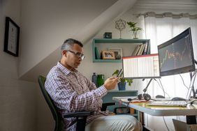 Man looking at currency trading app on his smart phone from his home officeMan looking at currency trading app on his smart phone from his home office