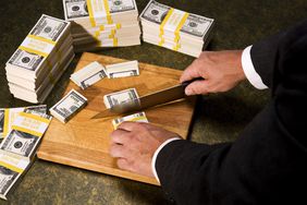 Person cutting up stacks of money using a sharp knife indicating a fiscal year budget