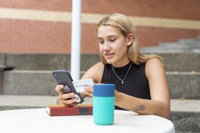 young woman in black tank top looking at phone with credit card