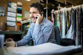 Happy mature businessman sitting at his desk talking on cordless phone. Fashion shop owner having telephonic conversation with client.