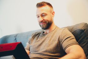bearded man reading from laptop on couch