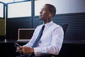 Man in dress shirt and tie sitting in office listening to phone through headphones