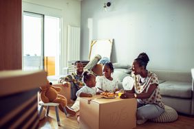 A family has breakfast seated on the floor of their new home with boxes
