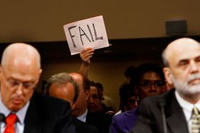 A demonstrator holds up a sign behind U.S. Treasury Secretary Henry Paulson (L) and Federal Reserve Board Chairman Ben Bernanke (R) during a hearing before the Senate Banking, Housing and Urban Affairs Committee