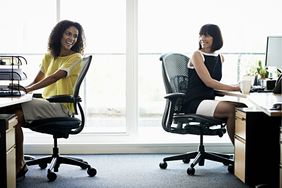 Two women laughing sitting in office chairs