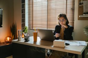 woman in blazer sitting at desk in front of computer in a dark room