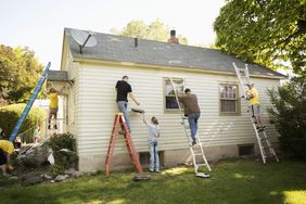 Four people paint the outside of a home.