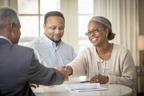 A smiling Black couple review paperwork with a mortgage broker.
