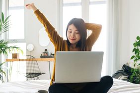 woman stretching while using laptop while sitting cross-legged