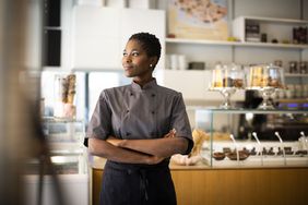 : Bakery owner with arms folded smiling and looking away