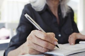 Mature woman writing in cheque book, mid section