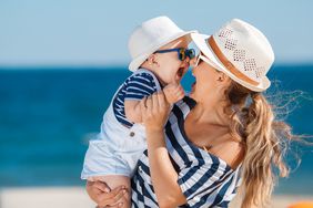 Laughing mother holding infant on summer beach vacation