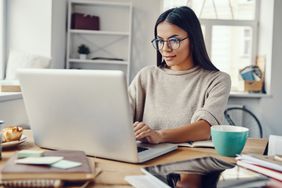 woman with long brown hair wearing glasses looking at computer