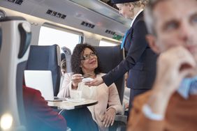 Woman with credit card using contactless payment, paying attendant on passenger train.