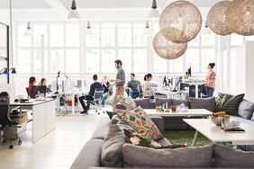 Office laborers sit at desks or mill about in an open concept working space.