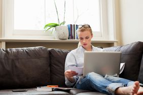 Young woman sitting on sofa with laptop and papers
